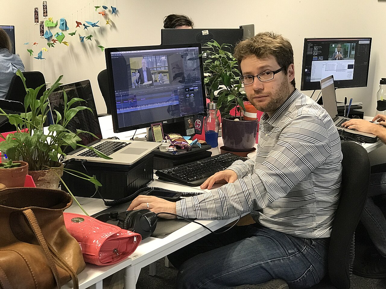 屋内オフィスで男性が動画編集ソフト画面を見ながらPC作業する様子