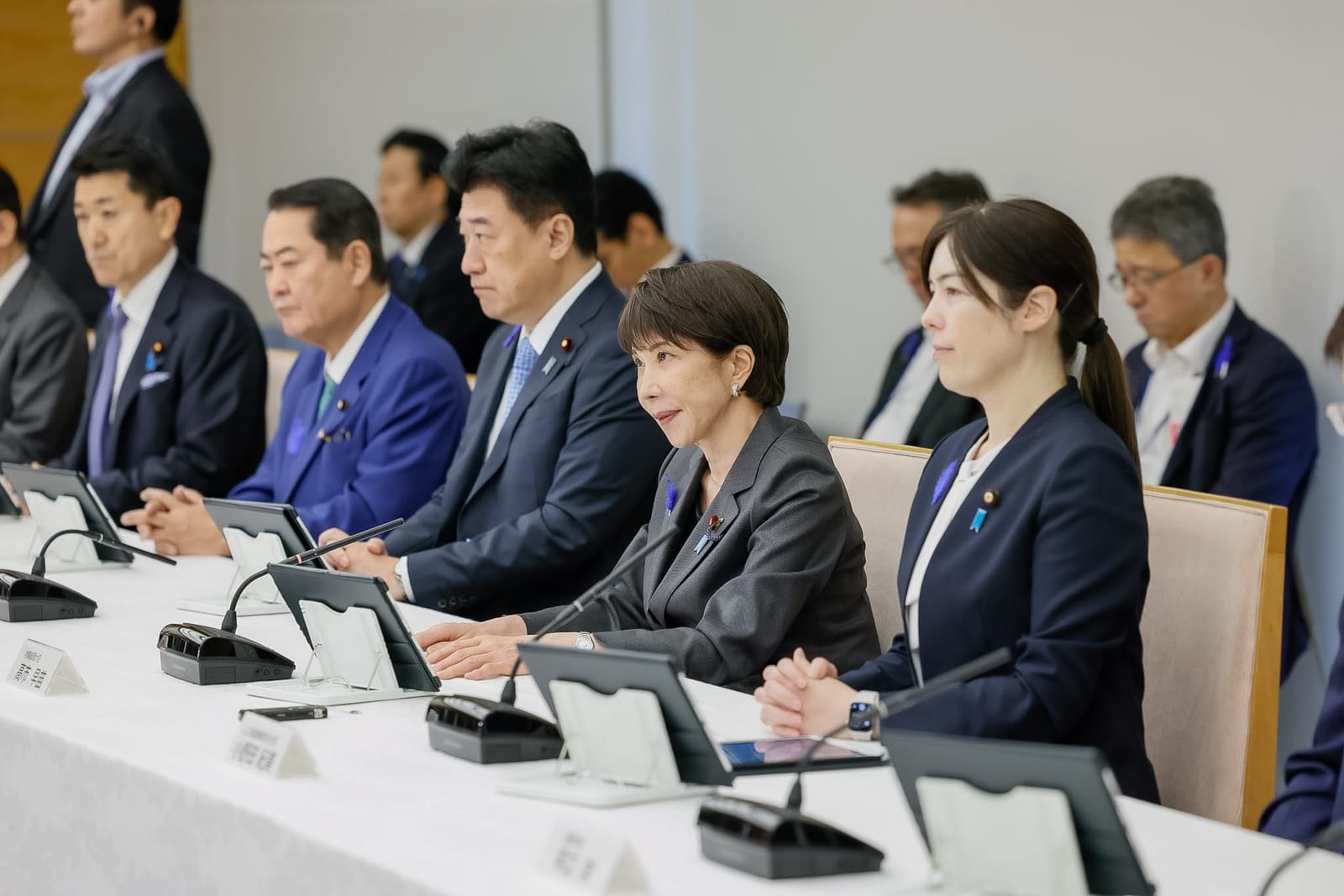 屋内の会議室で、テーブルに並んだ日本人の男女数名がタブレット端末を前に着席している様子