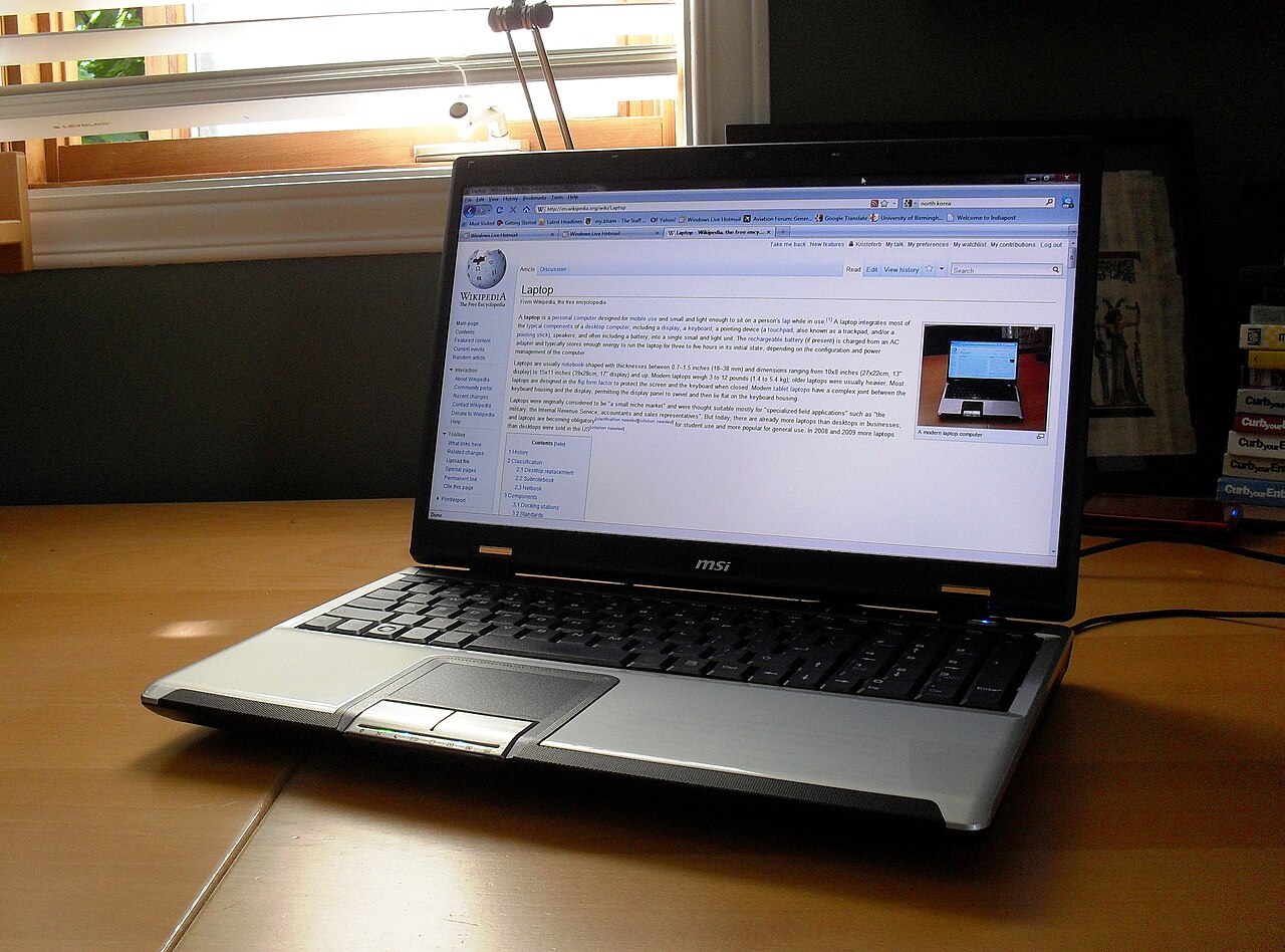 窓際の木製デスクに開いたノートPCが1台置かれている写真