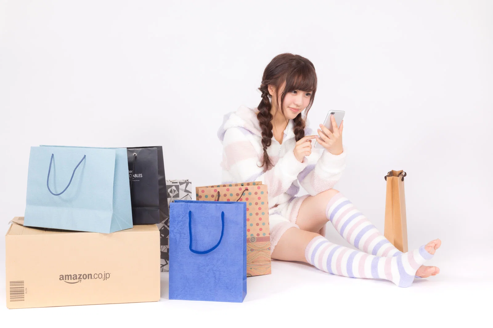 白背景の室内で、通販の紙袋や段ボールに囲まれ座る女性1人がスマートフォンを見ている。