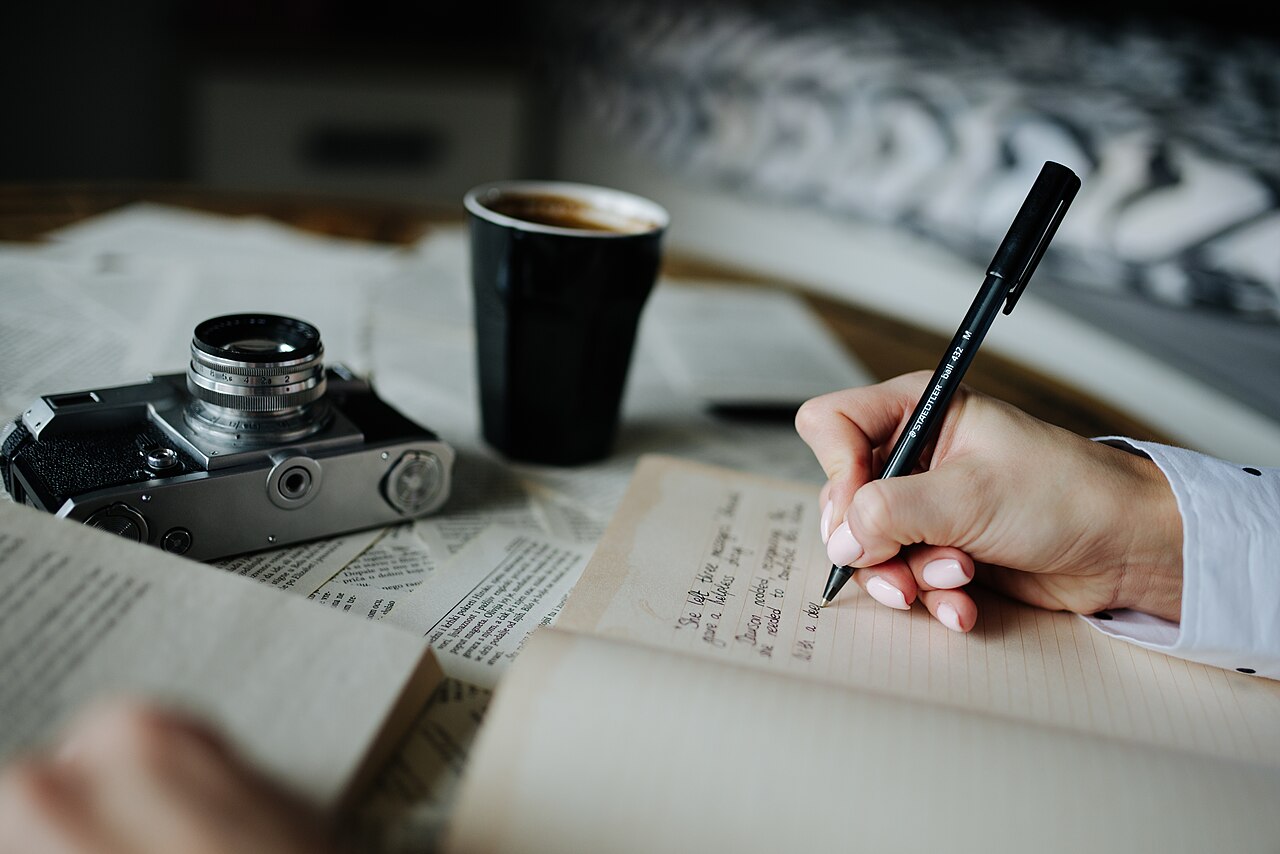 コーヒーを飲みながらノートに手書きでメモを取る人物
