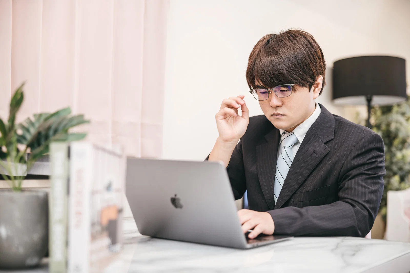 屋内でスーツ姿の男性1人がノートPCを操作し眼鏡に触れている