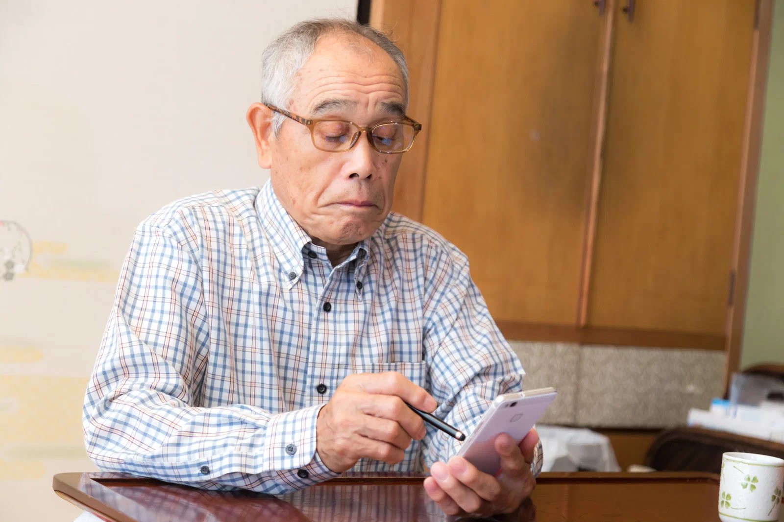和室でタッチペンを持ちスマートフォンを操作する高齢男性一人