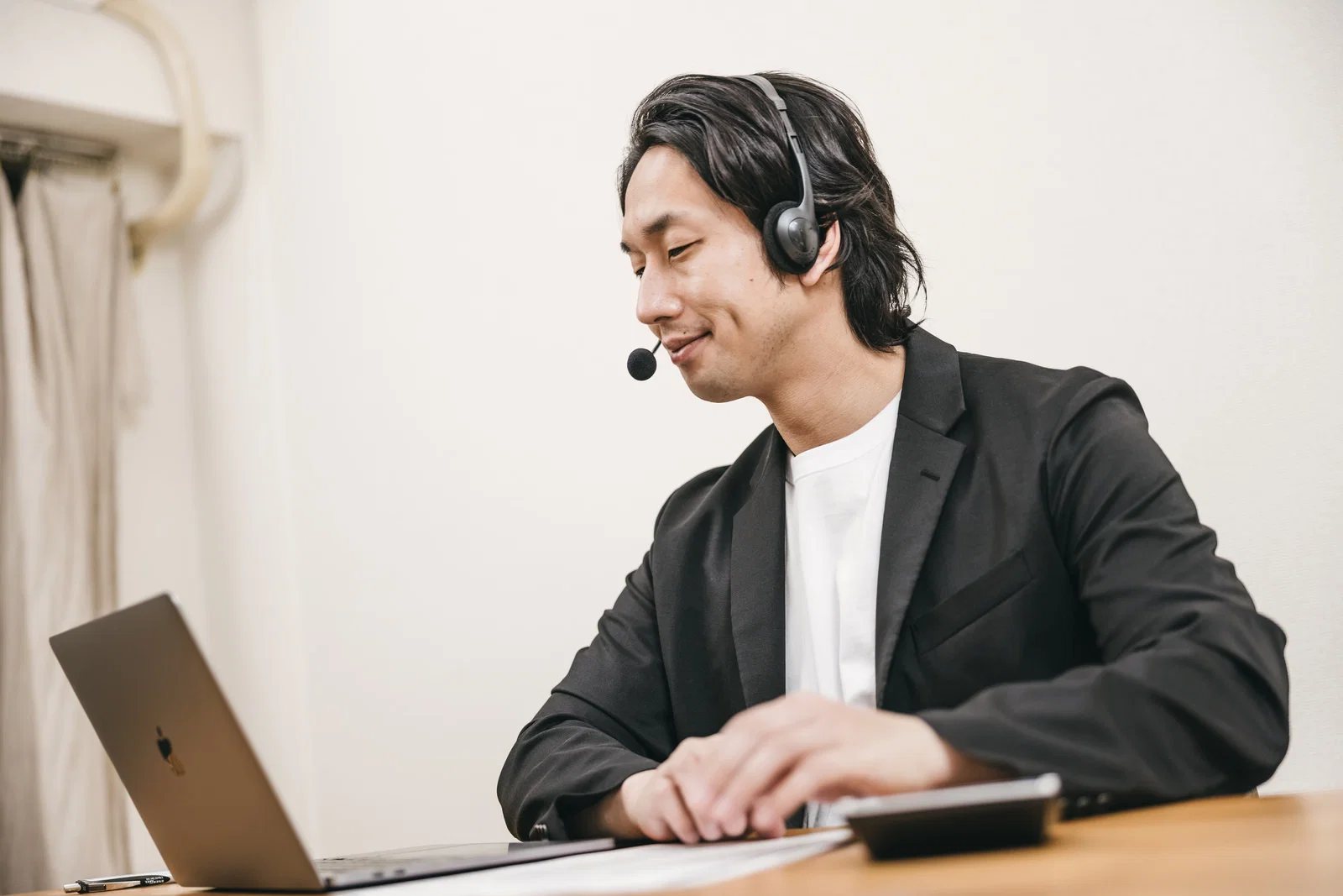 屋内で日本人男性1人がヘッドセットを着けノートパソコンに向かい話している
