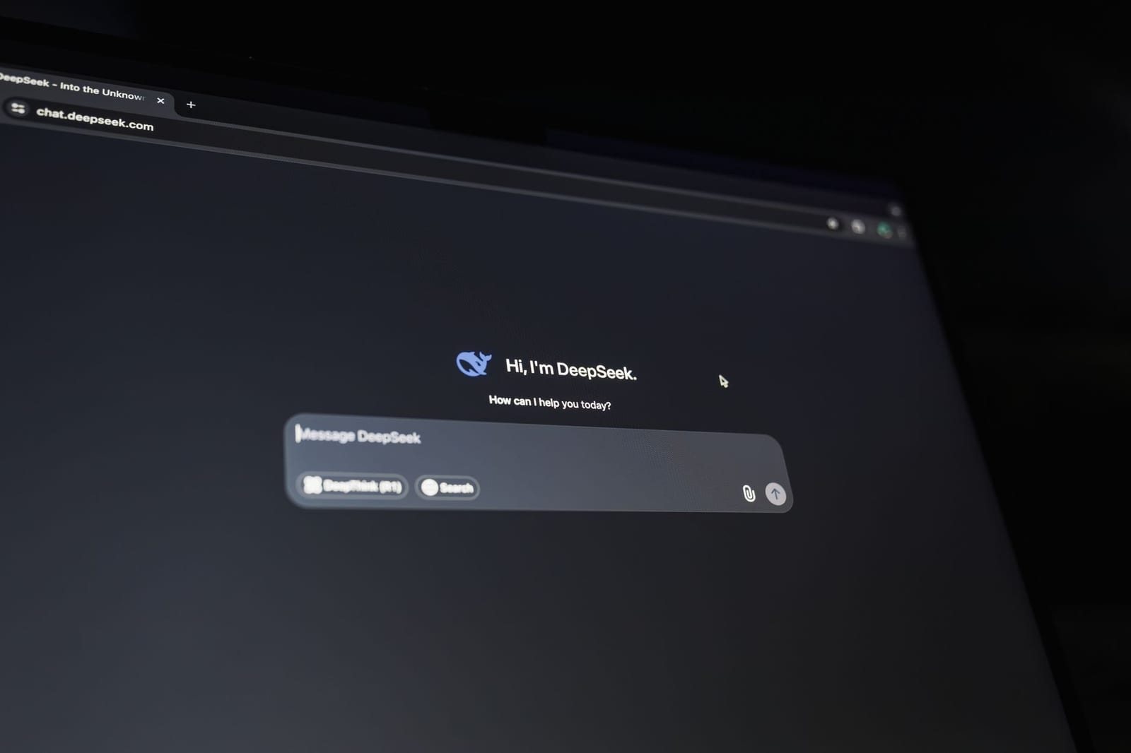 暗い室内でチャット画面「Hi, I'm DeepSeek.」を表示するノートパソコン画面の接写写真。