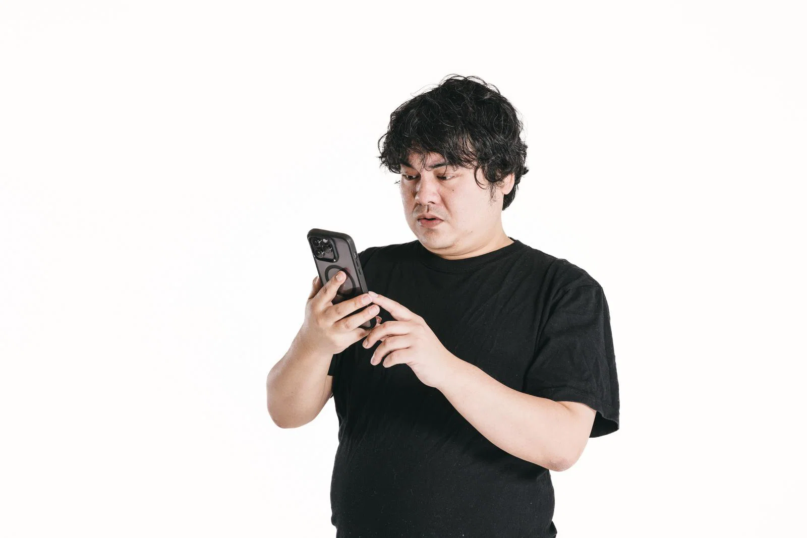 白背景に立つ黒シャツの男性1人が、手に持った黒いスマートフォンの画面を見ている写真。