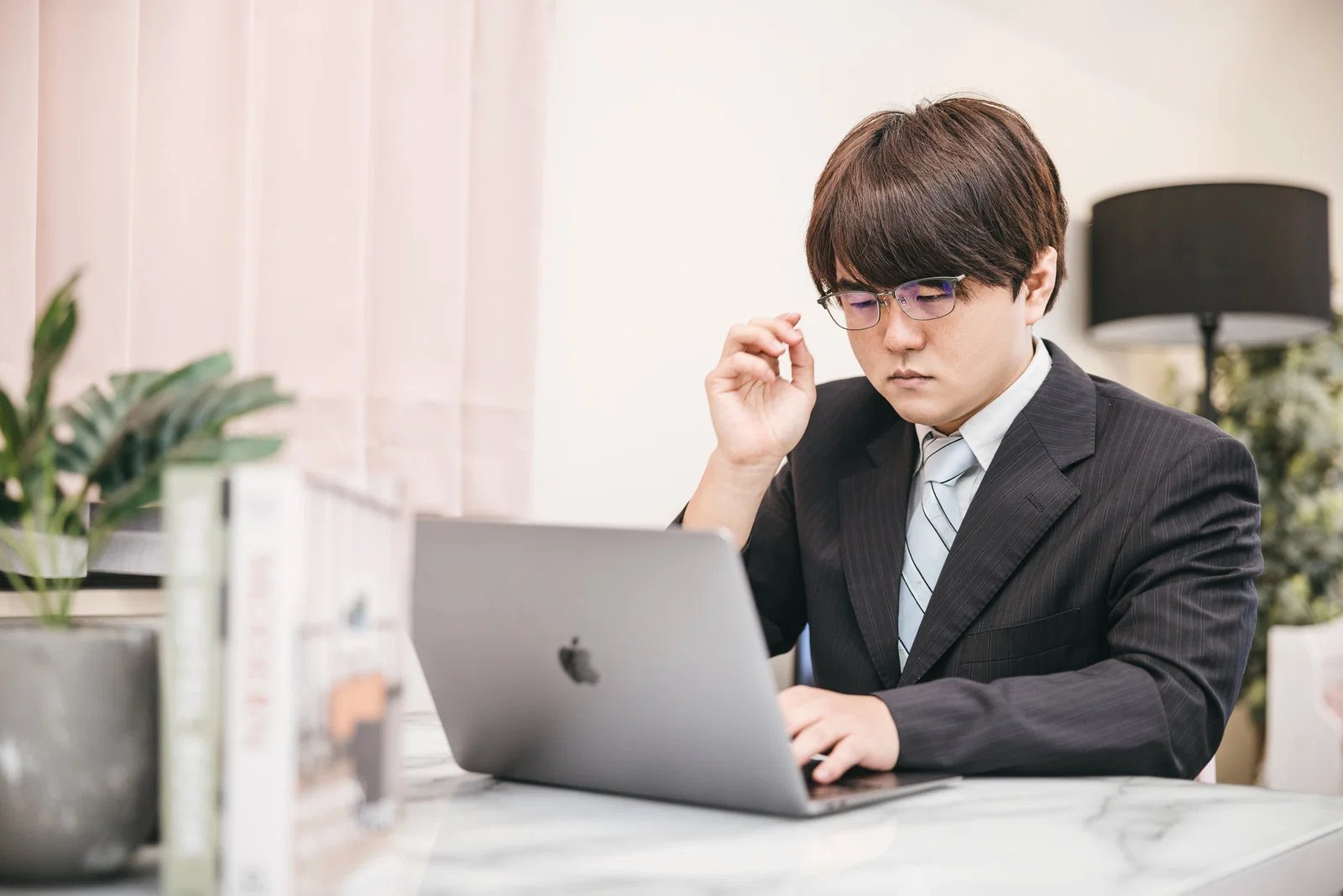 屋内オフィスでスーツ姿の男性1人がノートパソコンを操作している写真