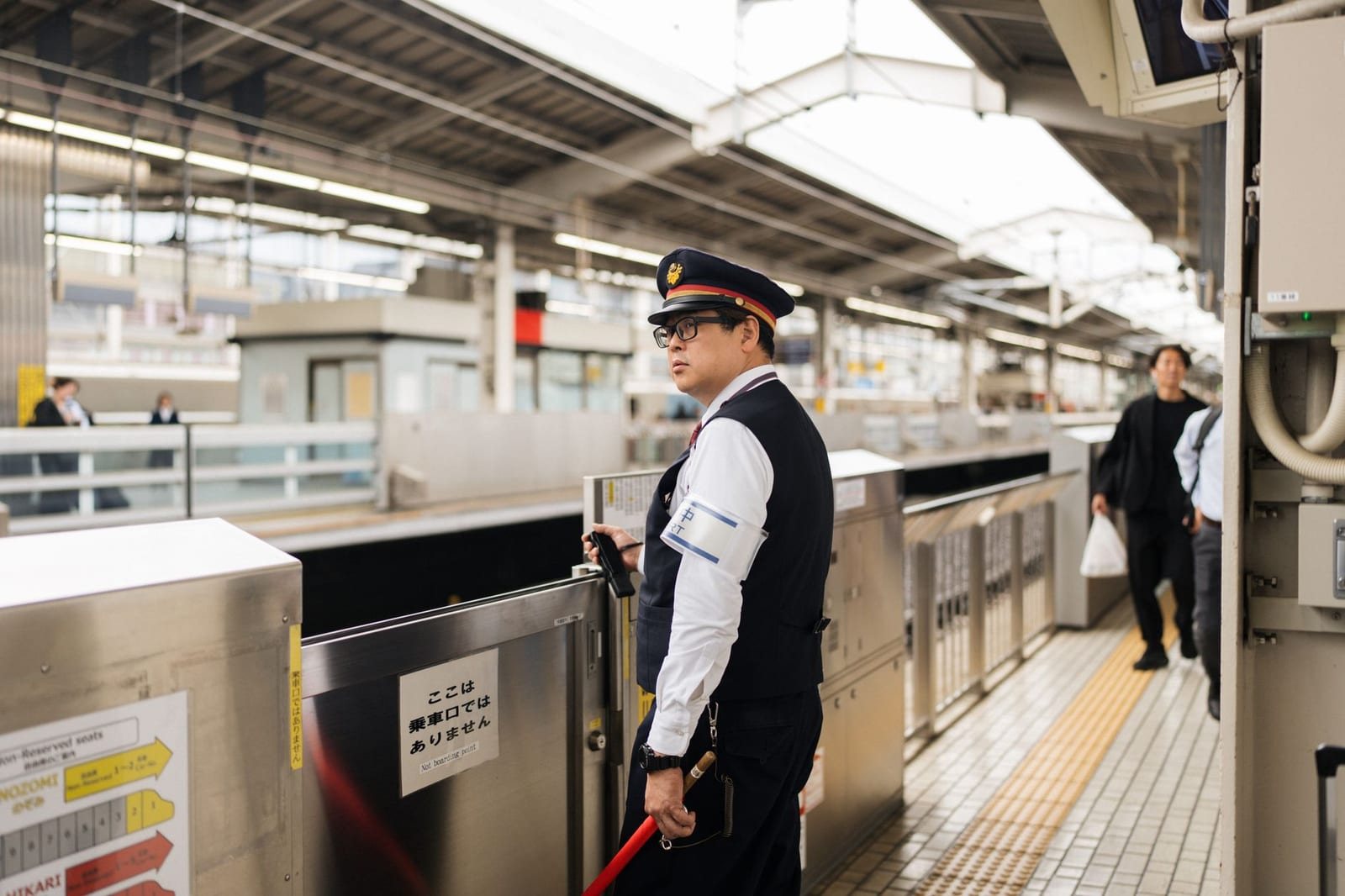 屋内駅ホーム、帽子姿の駅員1人と歩く乗客たち