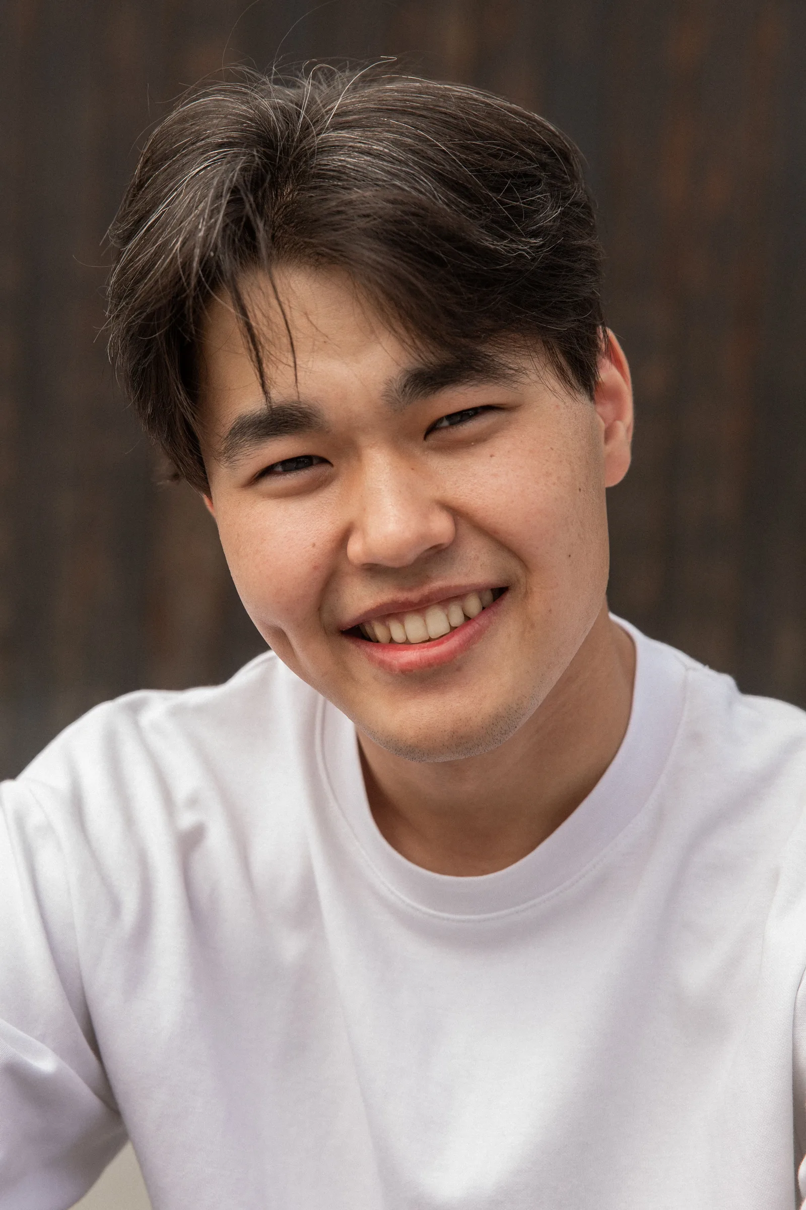 白いTシャツを着た若い男性が笑顔でカメラを向いているポートレート写真