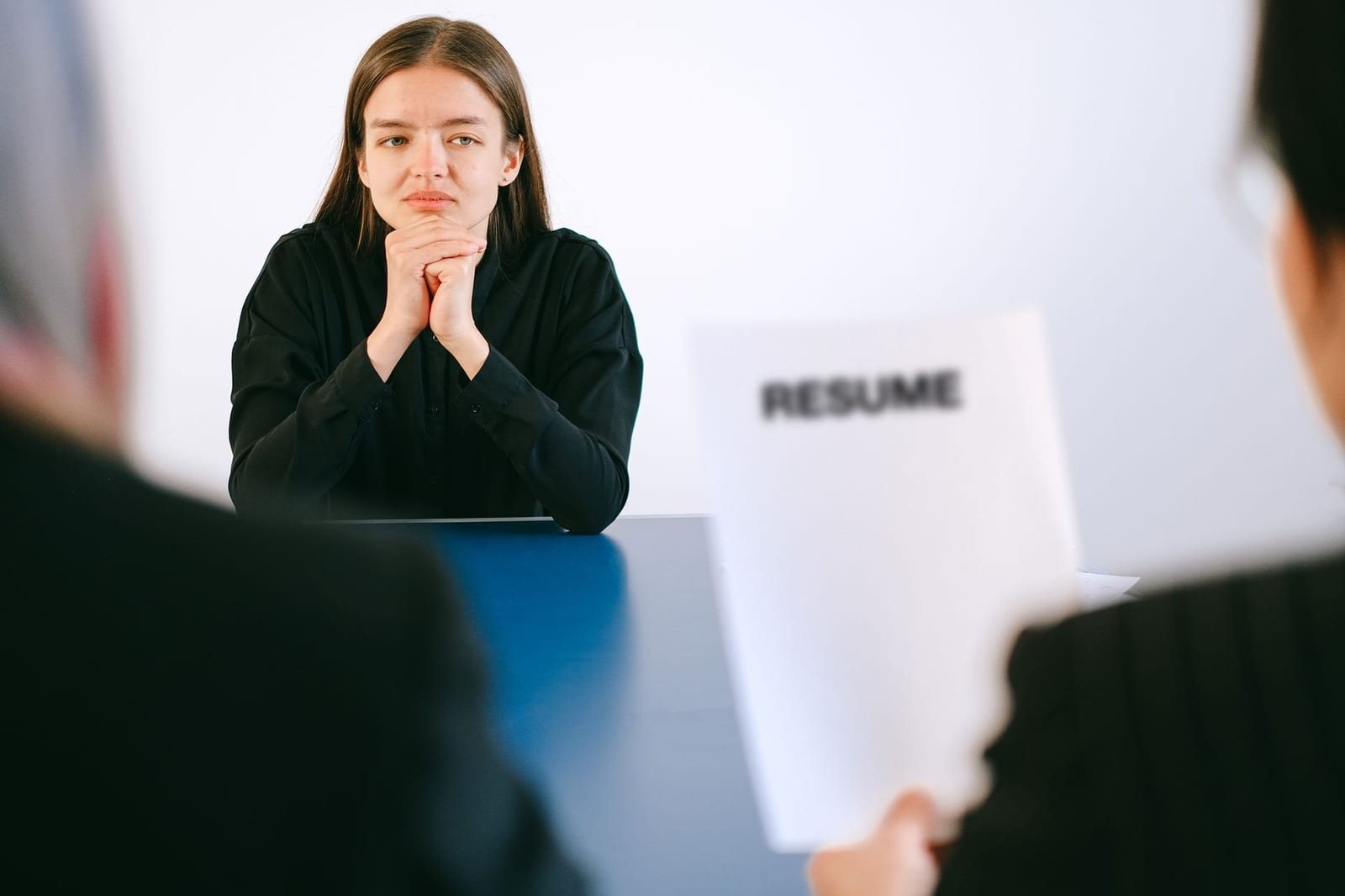 屋内で黒い服の女性が両手を組みRESUMEの紙を持つ人と向き合う面接風景