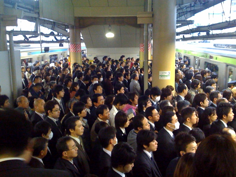 夏の東京、通勤ラッシュのホームに並ぶスーツ姿の会社員たち