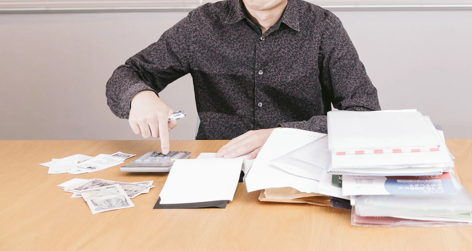 机で紙幣とレシートを前に電卓を操作する男性1人の上半身