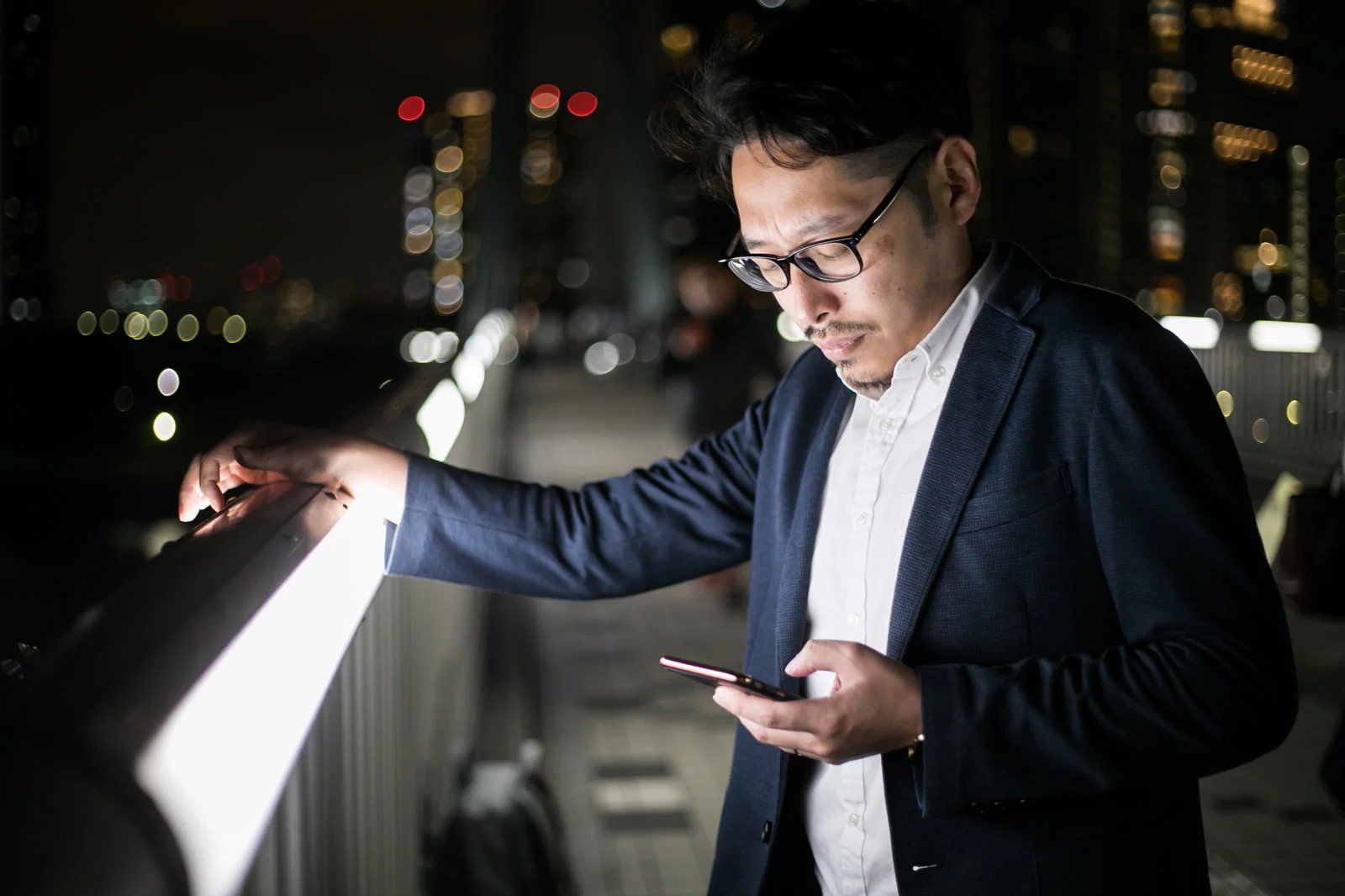 夜の屋外で男性1人がスマートフォンを見ている様子