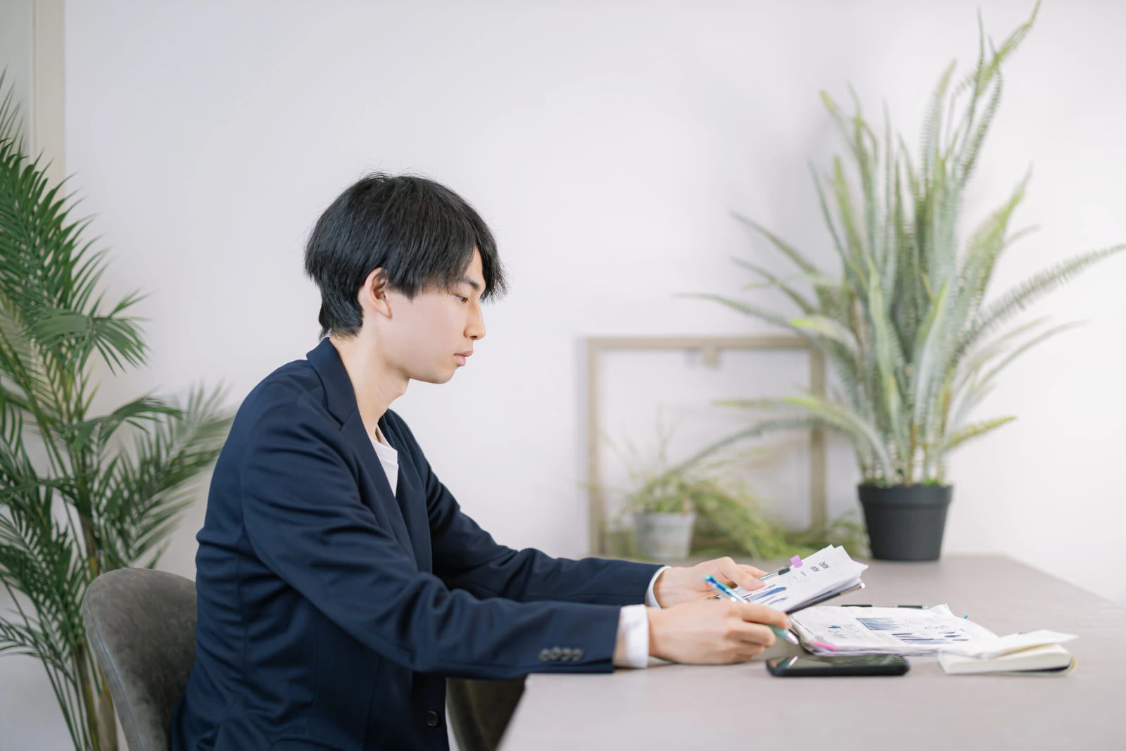 観葉植物のある室内で、書類を手にスーツ姿の男性1人が座って確認している