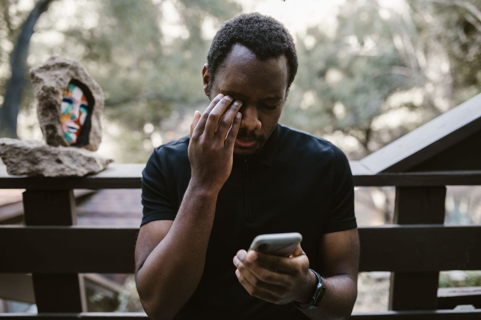屋外のベランダでスマートフォンを見ながら目を拭う男性
