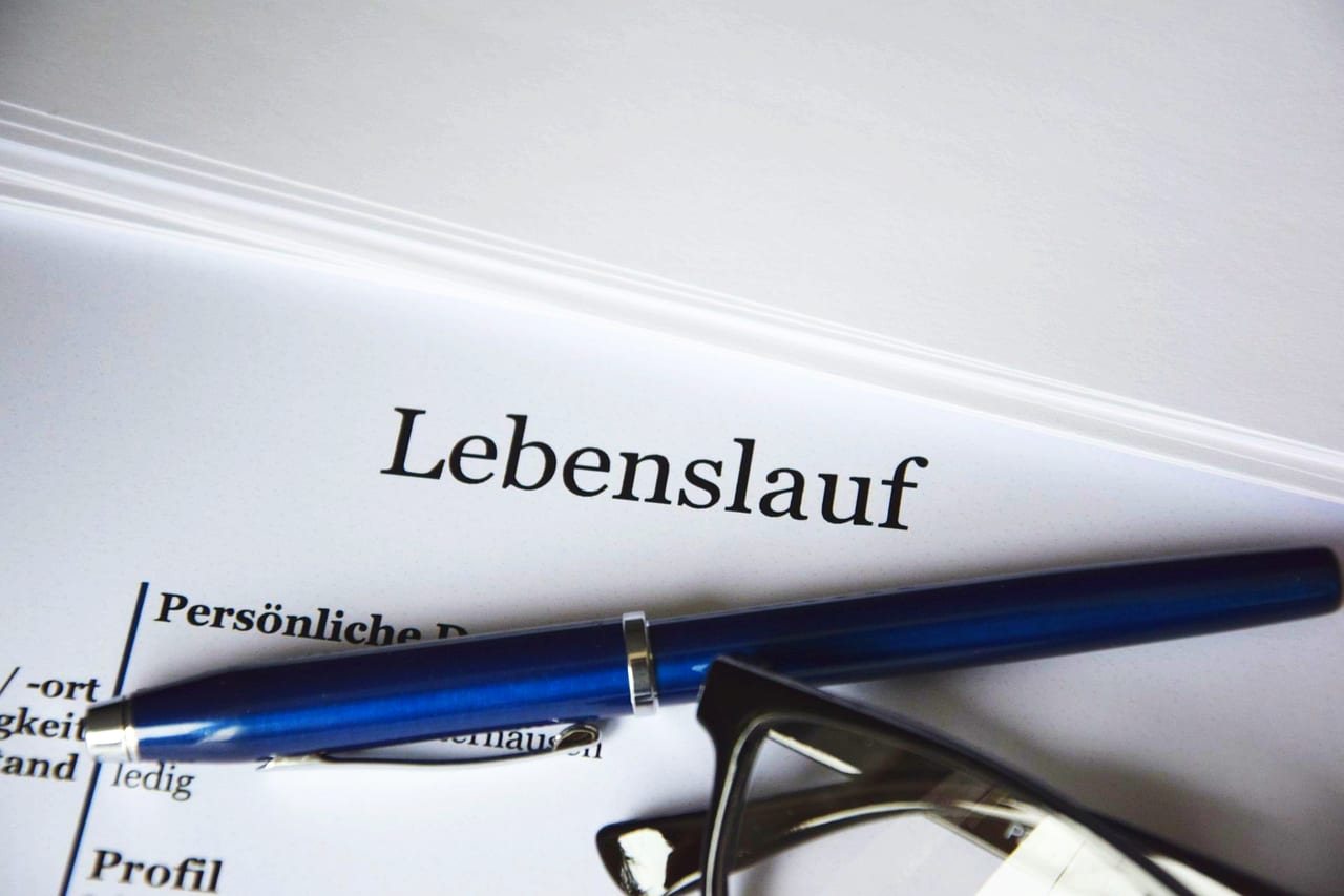 「Lebenslauf」の文字が印刷された書類にペンと眼鏡が置かれた写真