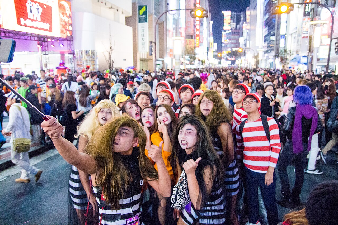 仮装した大勢の人が夜の路上でスマホを掲げて自撮りする様子