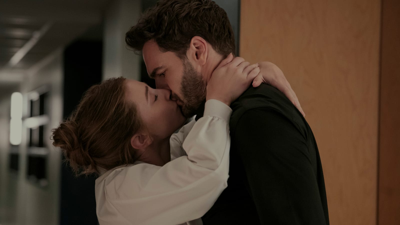 屋内の廊下で男女2人が抱き合いキスをしている場面