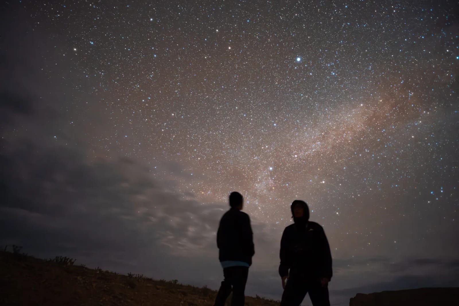 丘の上で2人が並んで天の川の見える夜空を見上げている屋外の写真