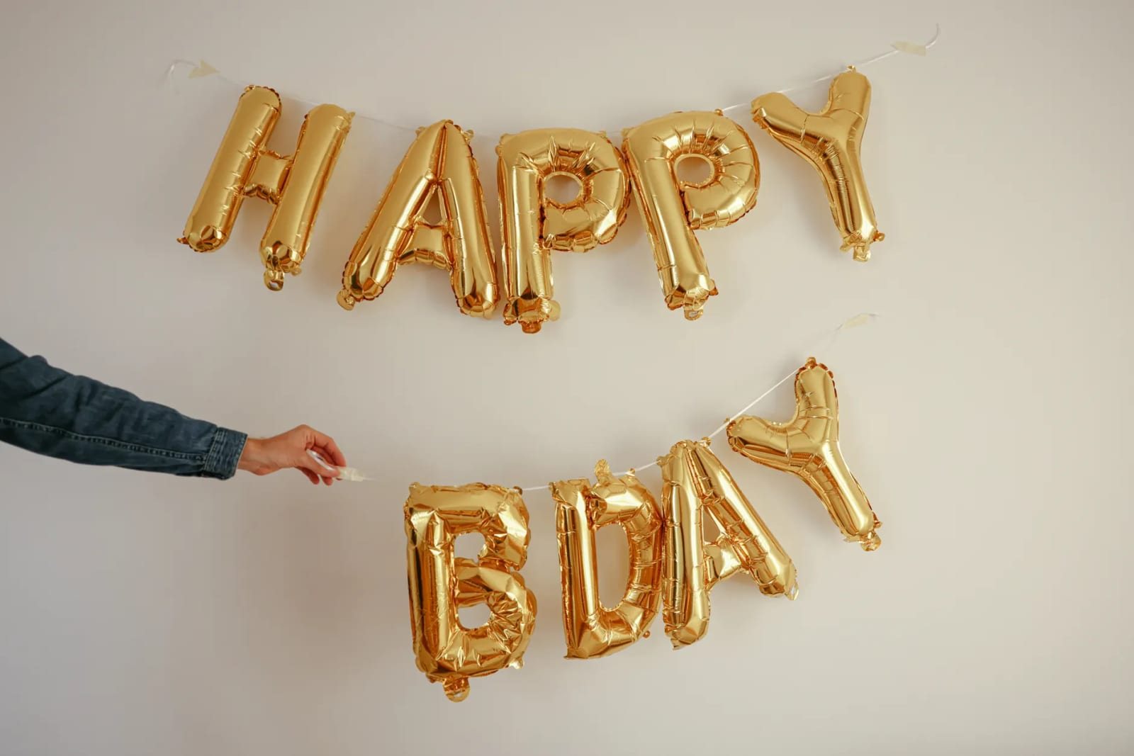 壁に金色のHAPPY BDAY風船文字を人の手が飾り付ける写真