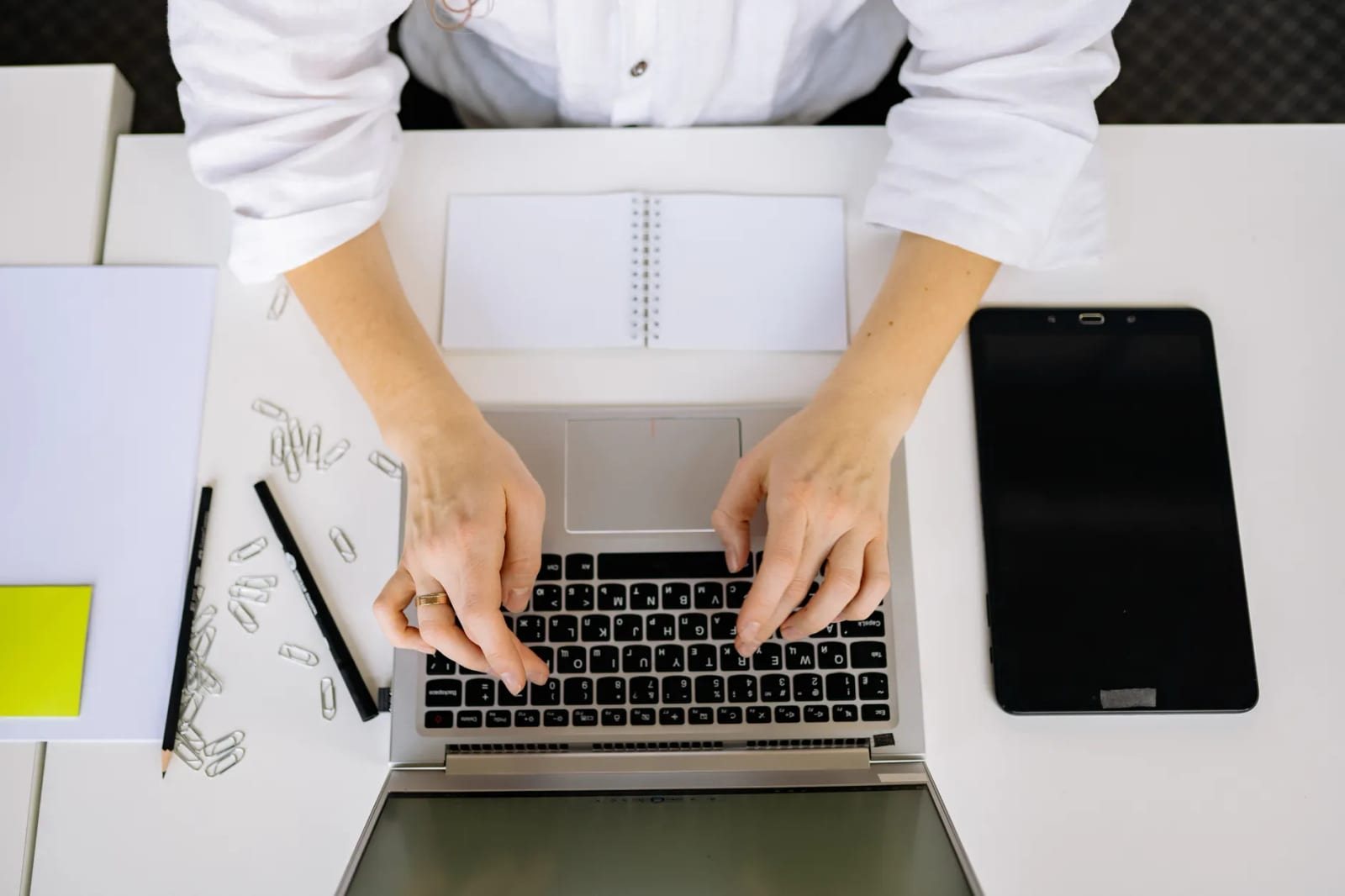 白いデスクで白シャツの人物が両手でノートPCのキーボードを操作している
