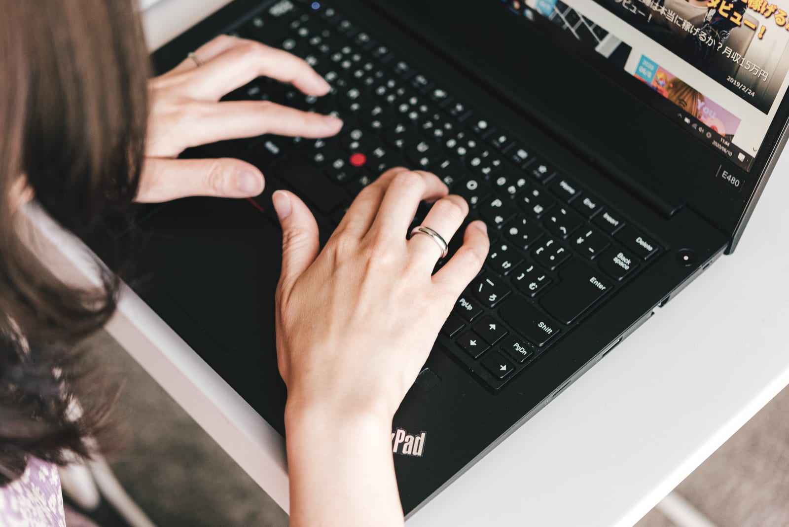 屋内のデスクでノートパソコンのキーボードを操作する女性の手元のアップ