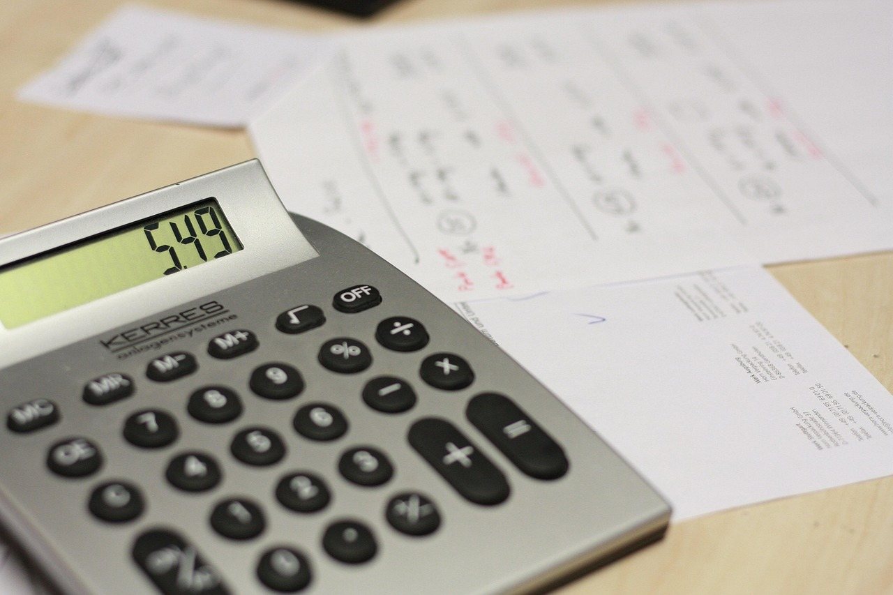 木製の机に置かれた電卓の液晶に549の数字が表示され書類が広がる接写