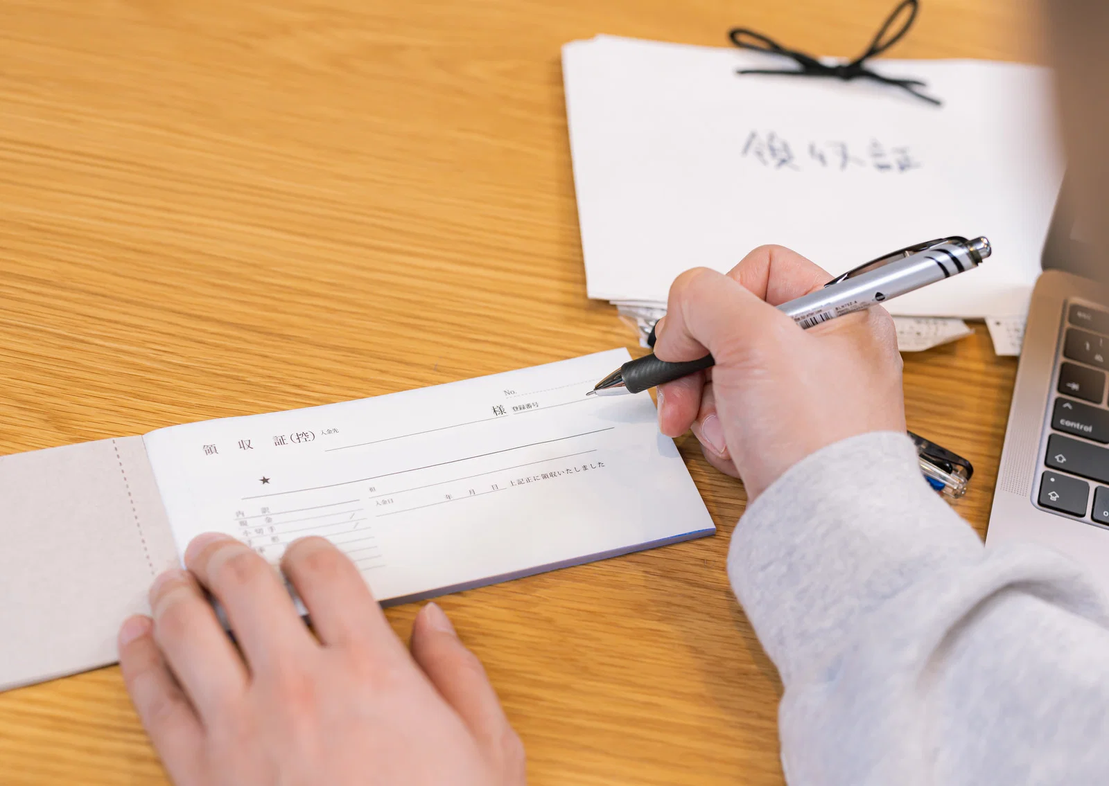 屋内の木製デスクで、1人が手書きの領収証控えにペンで記入している様子