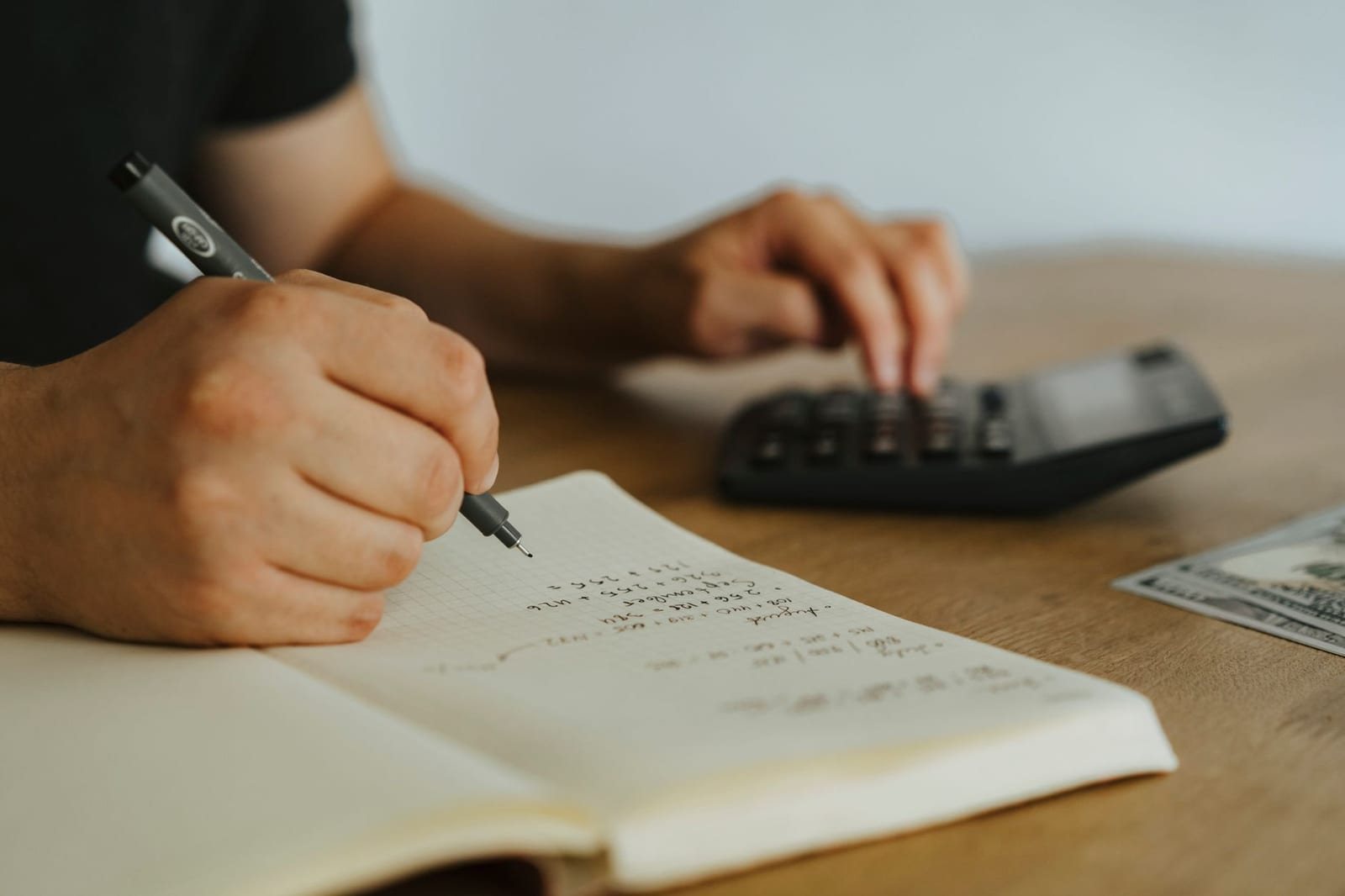 机でノートに書き込みながら電卓を操作する人の手元