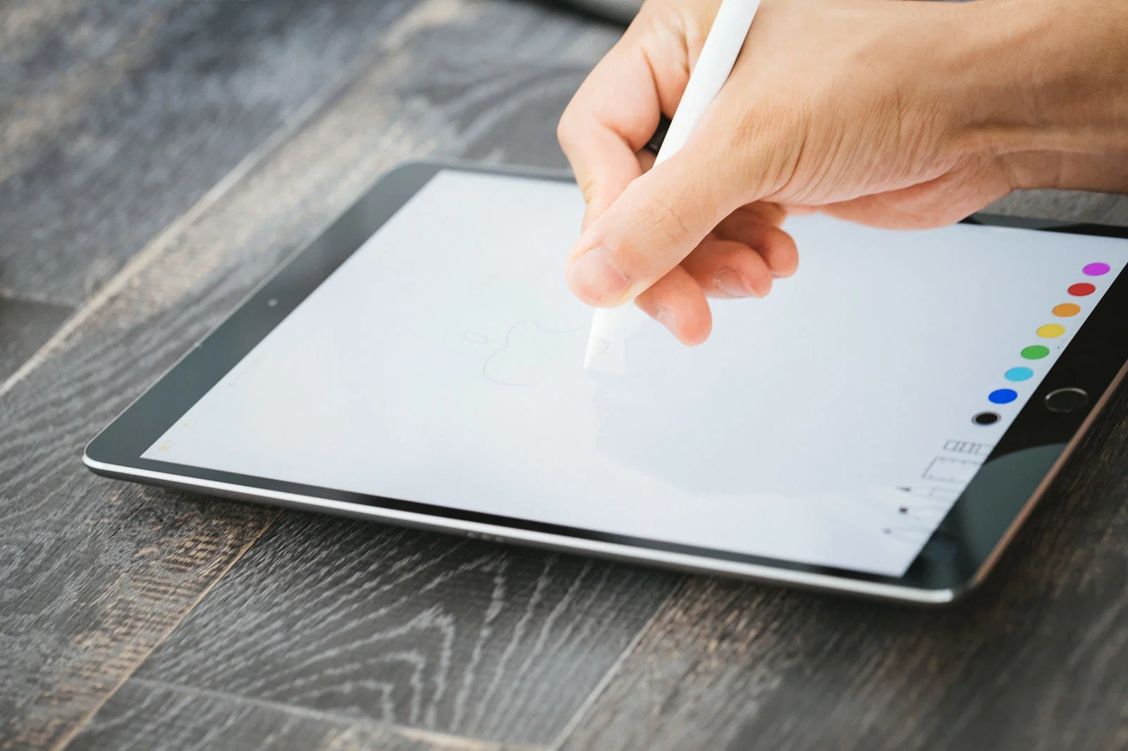 室内の木目テーブルでタブレットにタッチペンでイラストを描く手元のアップ。