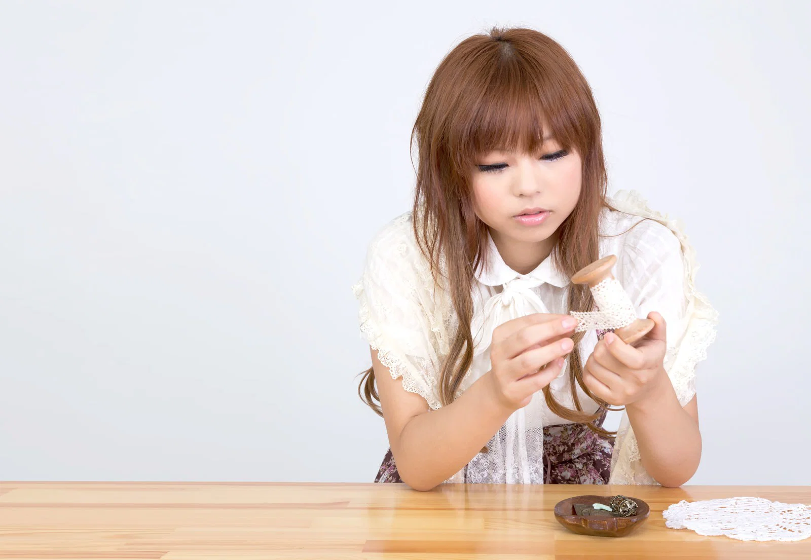 室内の木製テーブルで女性1人が木製のボビンに手作業でレースを巻いている様子