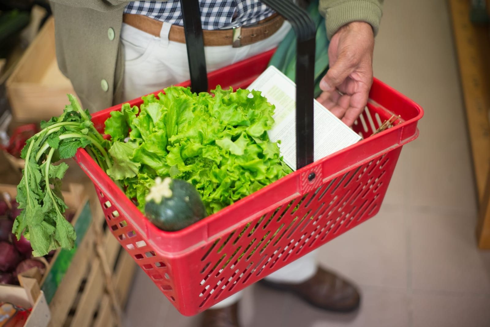 屋内で人物が野菜を入れた赤い買い物かごを持っている様子