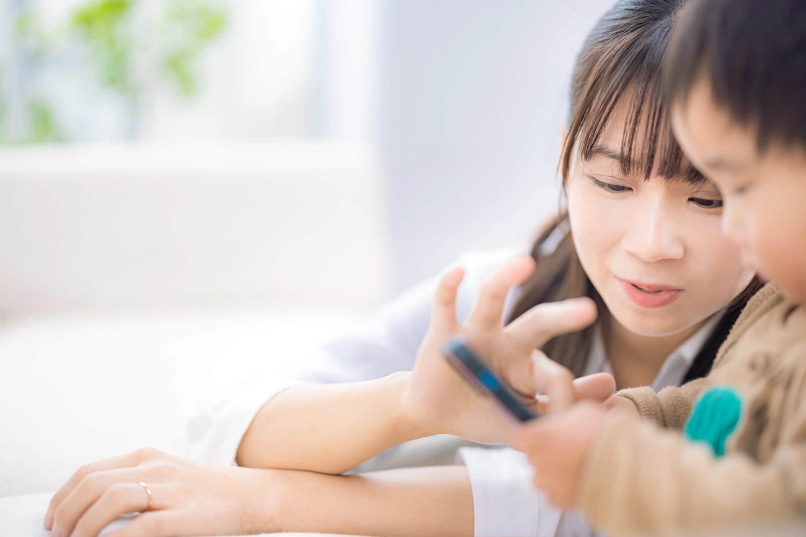 室内で女性と子どもが並んでスマートフォンの画面を一緒に見ている