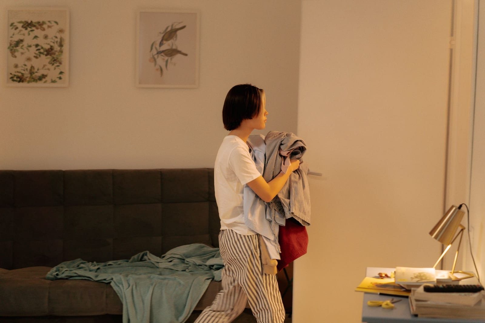 屋内リビング、洗濯物を抱えて歩く女性1人と絵画が飾られた壁、ソファ。