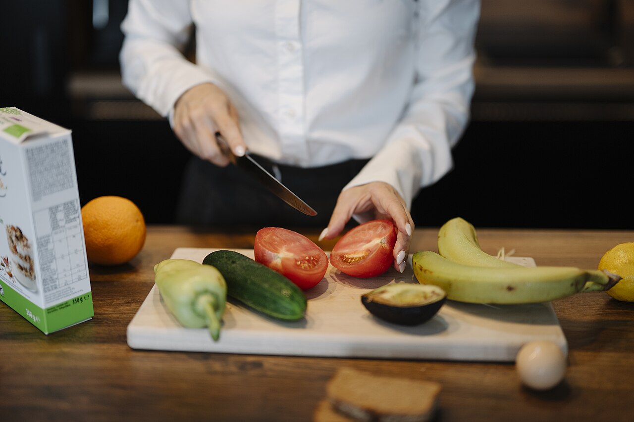 屋内の台所でトマトなど野菜と果物を包丁で切る人物の手元