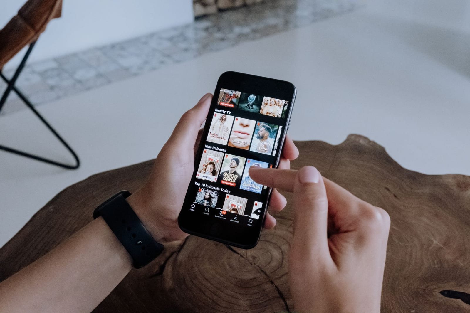 室内のテーブル上でスマートフォンの動画配信アプリ画面を両手で操作している写真