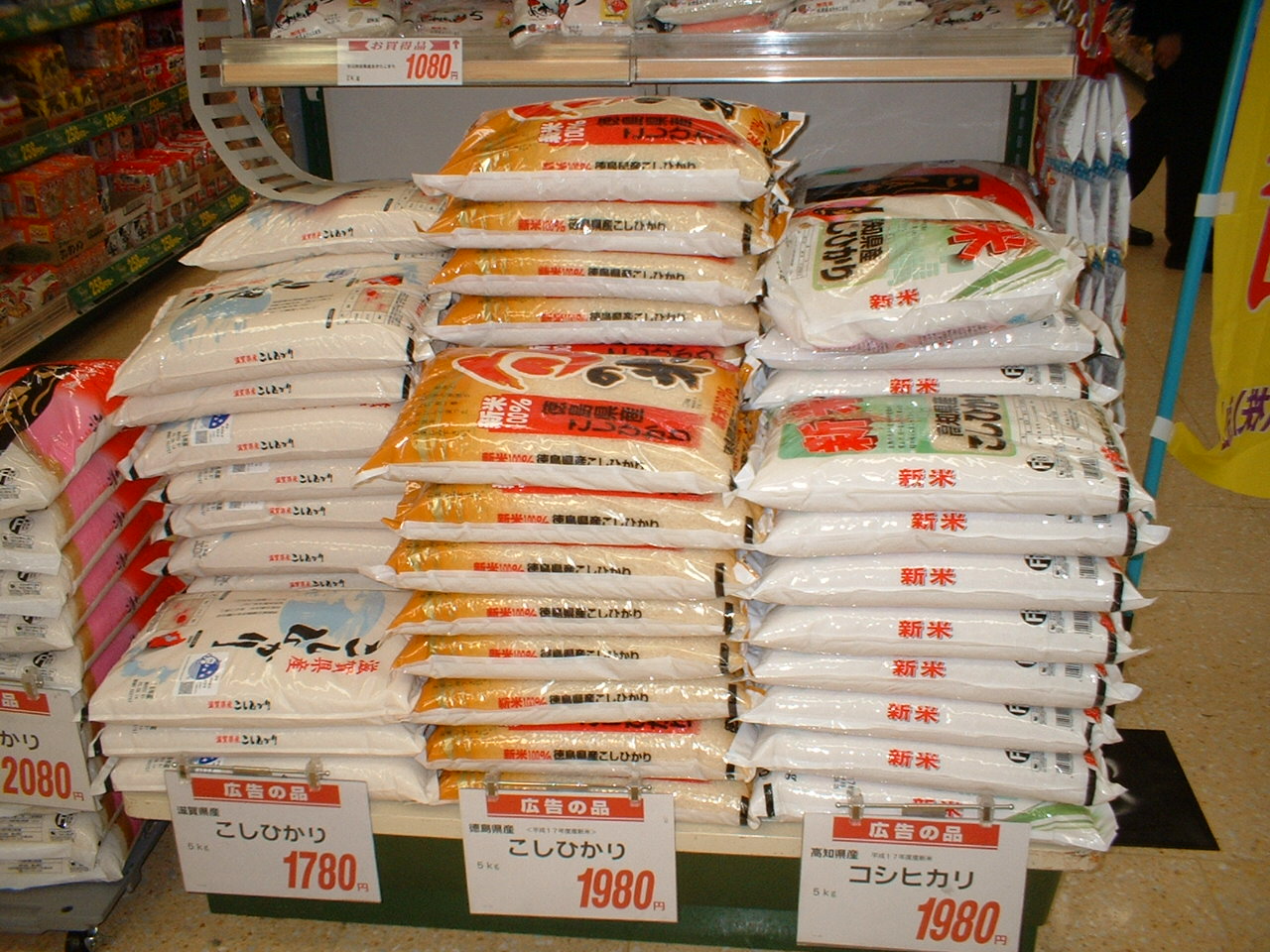 スーパー店内に米袋が種類別に山積みされ値札が付いた売り場