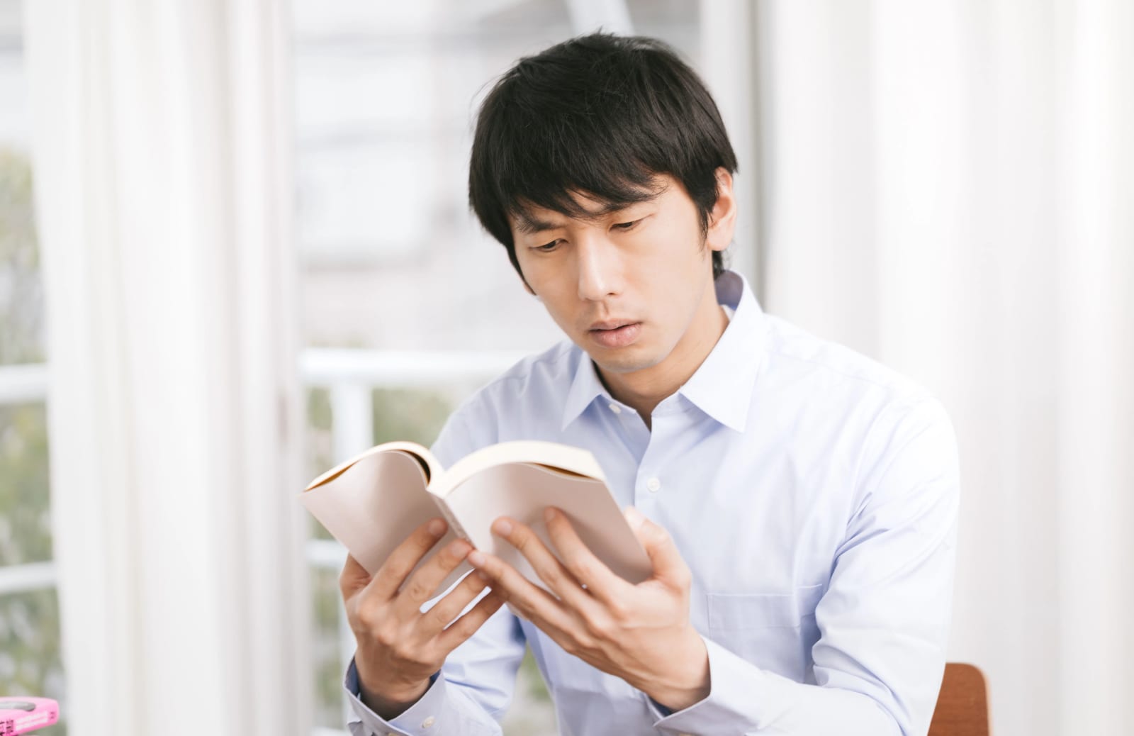 室内でワイシャツ姿の男性一人が椅子に座り本を開いて読んでいる