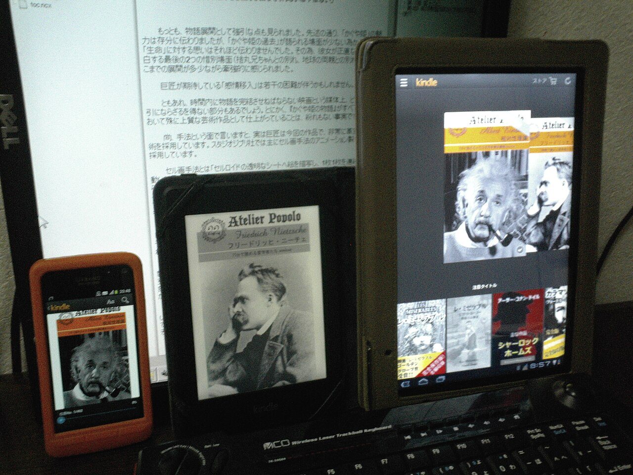 屋内の机にスマホ・電子書籍端末・タブレットが並び電子書籍が表示された写真