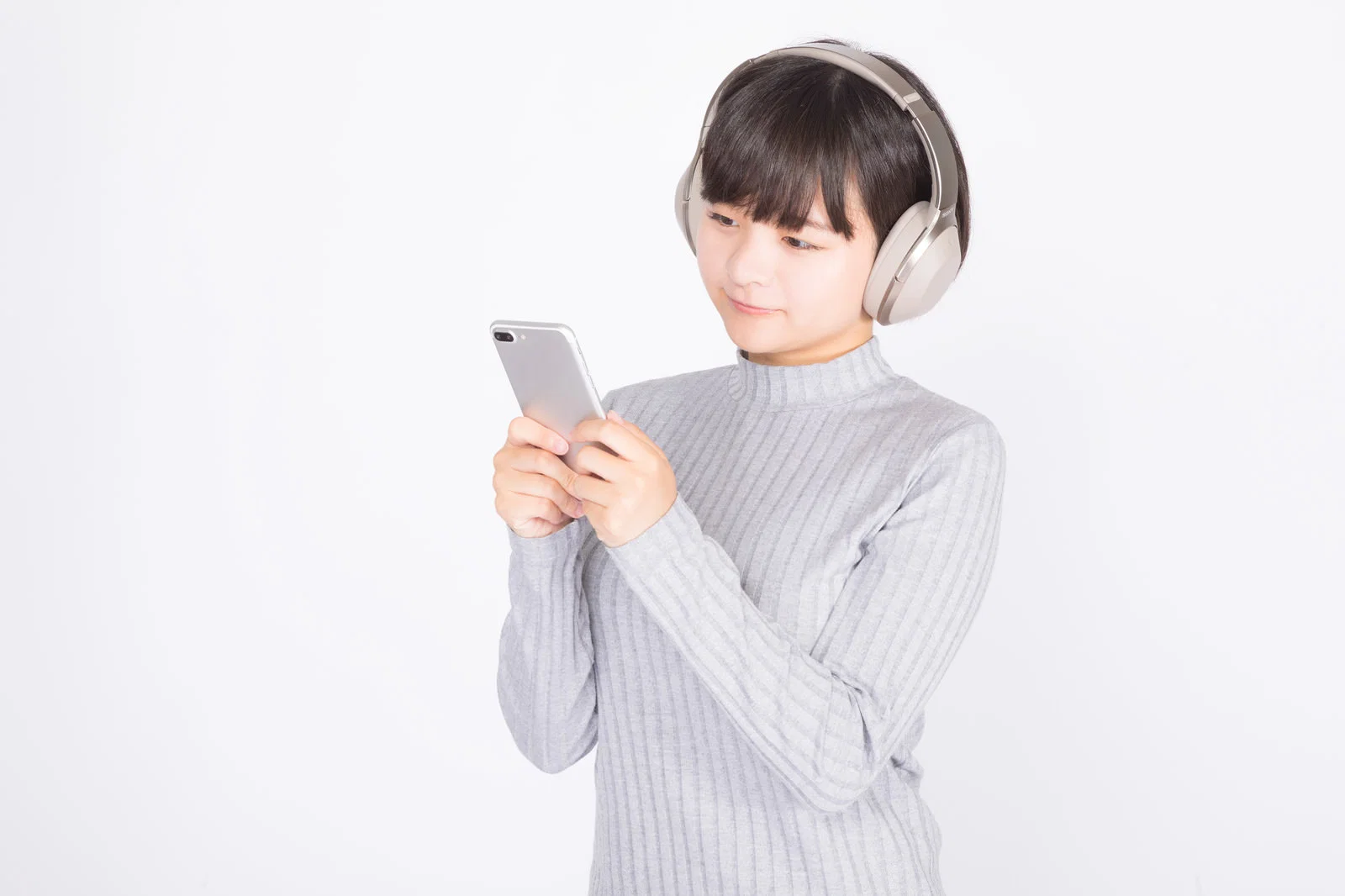 白背景の室内でヘッドホンをつけスマートフォンを操作する女性1人