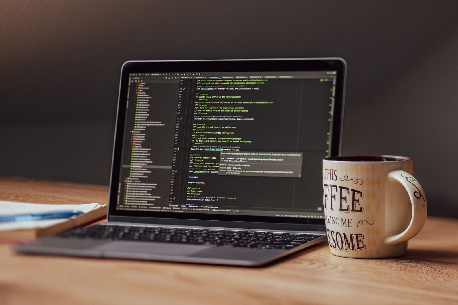 木製机の上でコード画面を開いたノートパソコンとコーヒーマグ