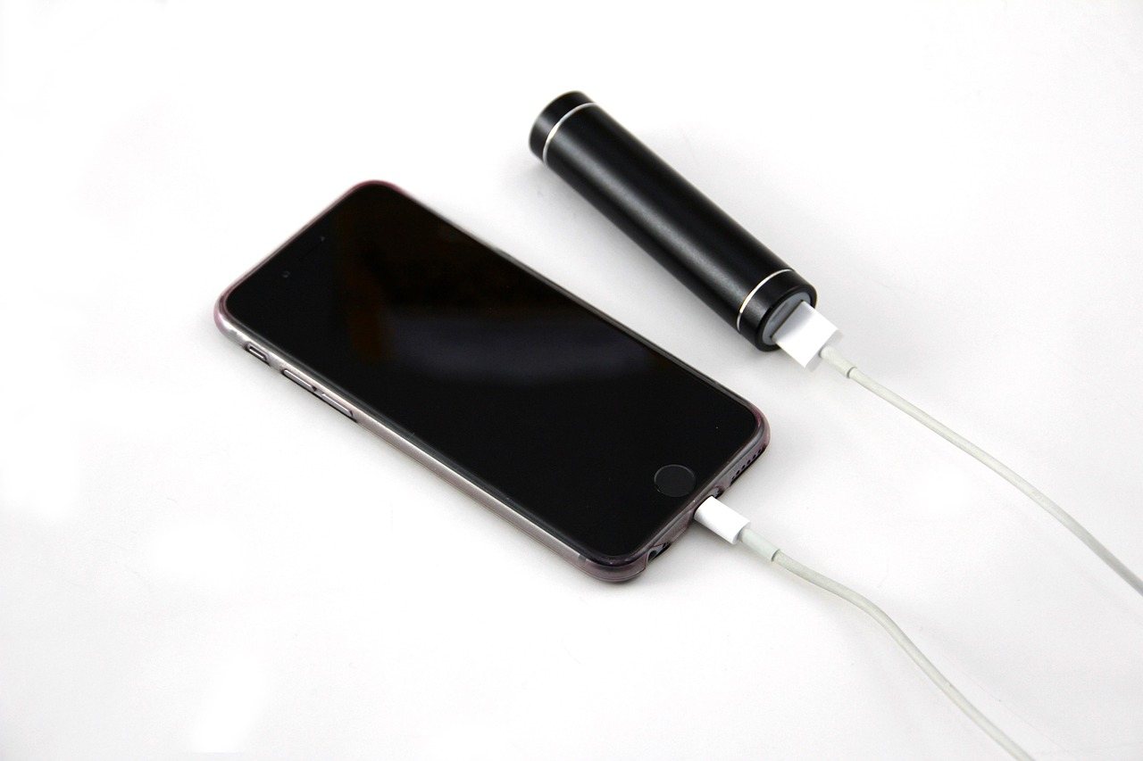 白背景でスマートフォンと黒い円柱型モバイルバッテリーがケーブルで接続された写真