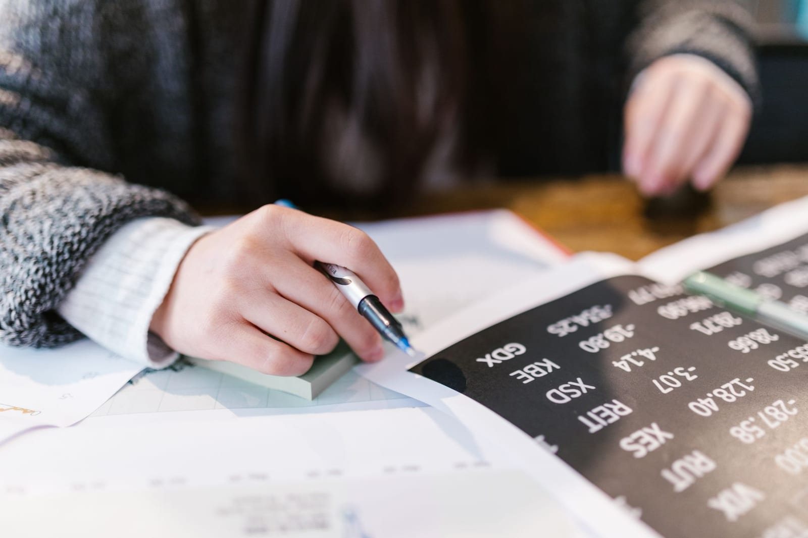 机で株価一覧の資料にペンで書き込む人物の手元