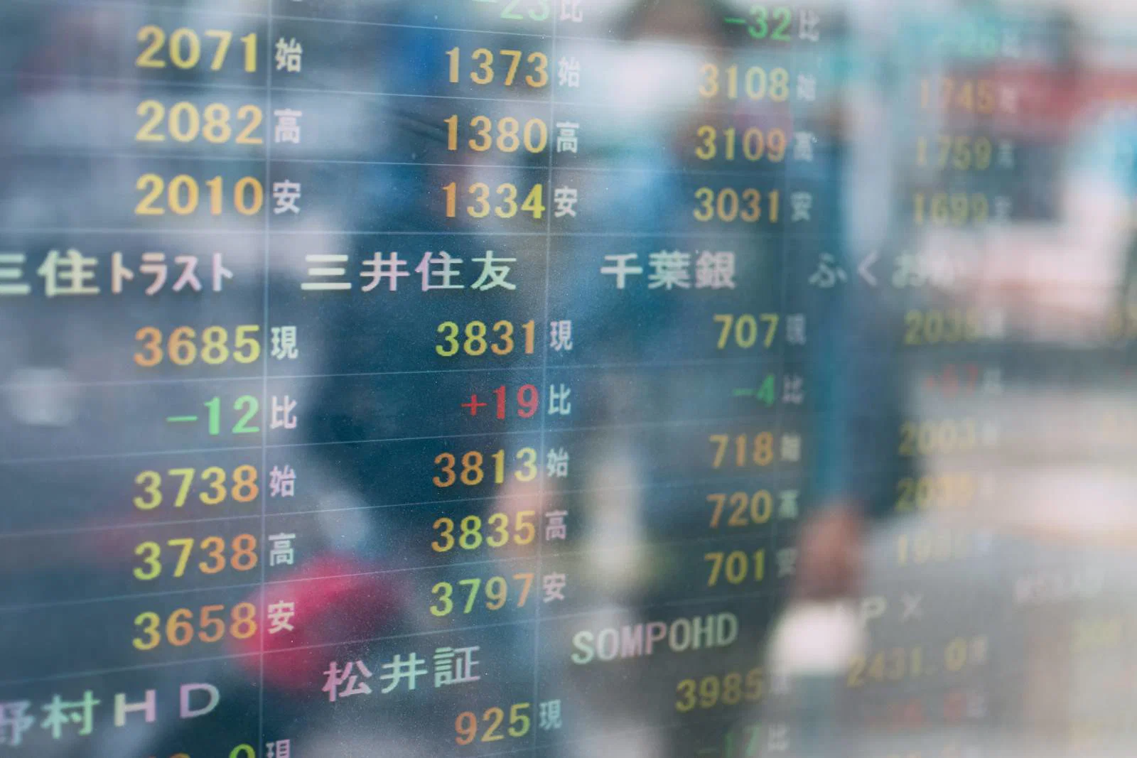 屋外の株価表示ボードに映る数字と通行人のシルエット