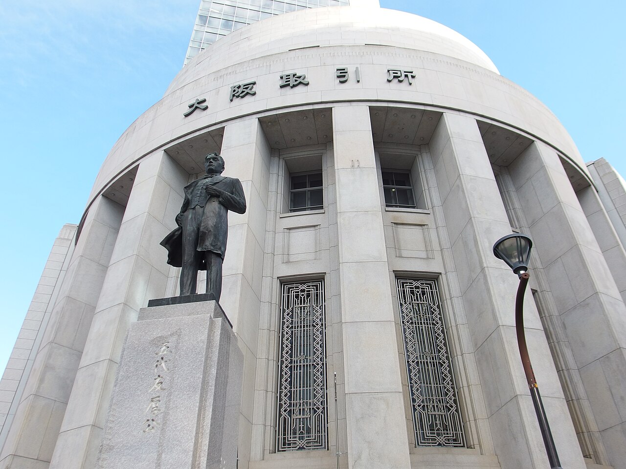 大阪取引所の円形の石造建築を青空を背に見上げた外観写真。左手前に五代友厚公の銅像が立つ