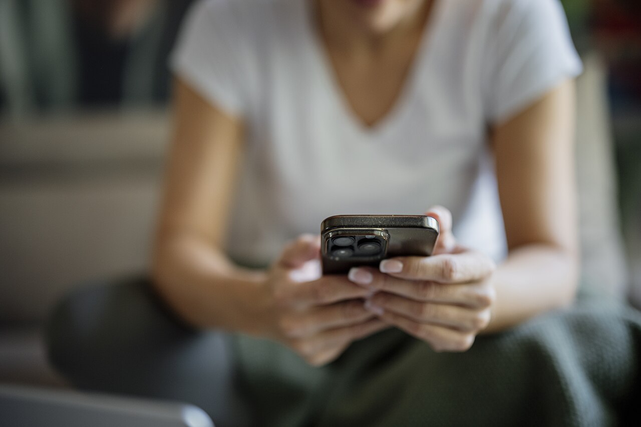室内でソファに座り、両手でスマートフォンを操作する女性のアップ