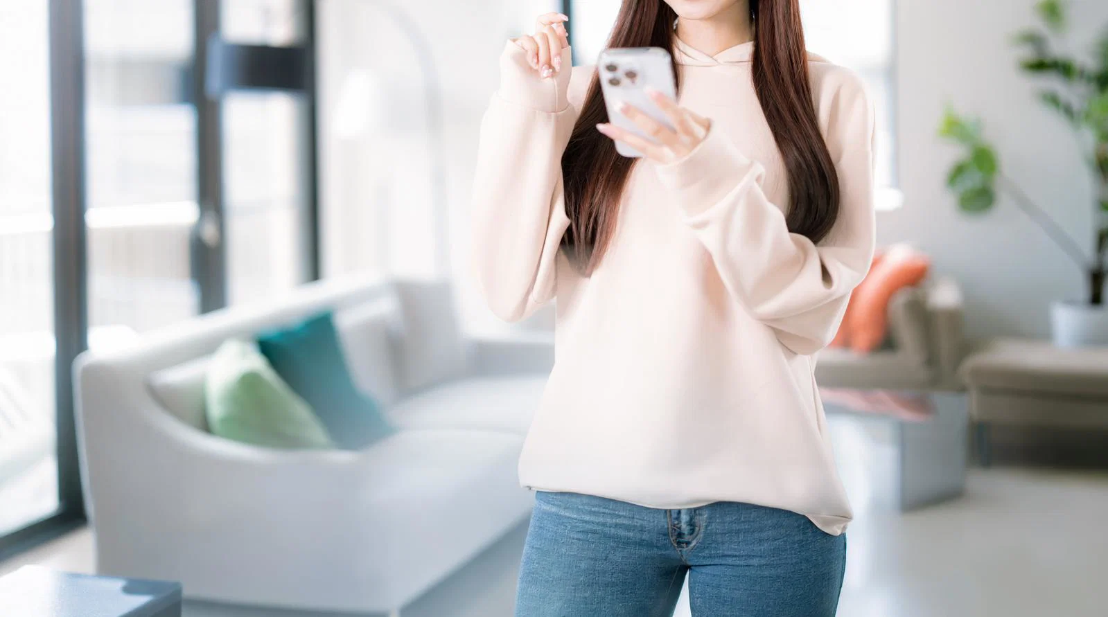 屋内のリビングで女性がスマートフォンを片手に操作している上半身の写真