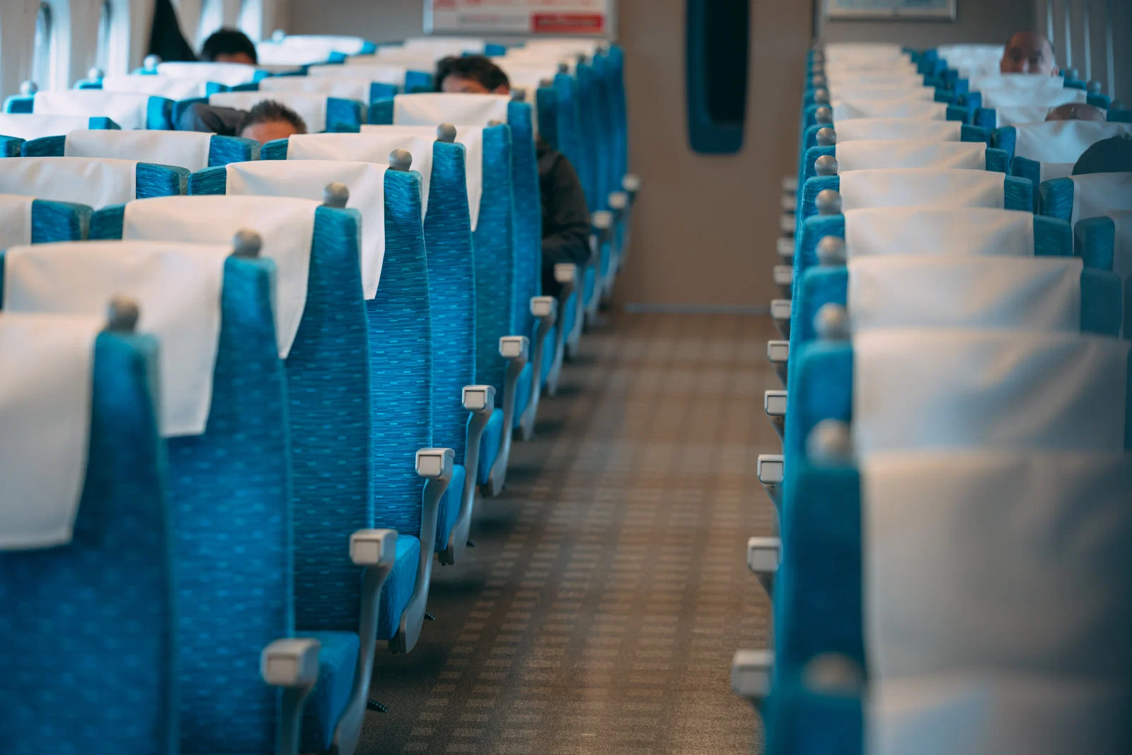 新幹線車内、青いリクライニングシートが並ぶ通路に数人の乗客が座っている