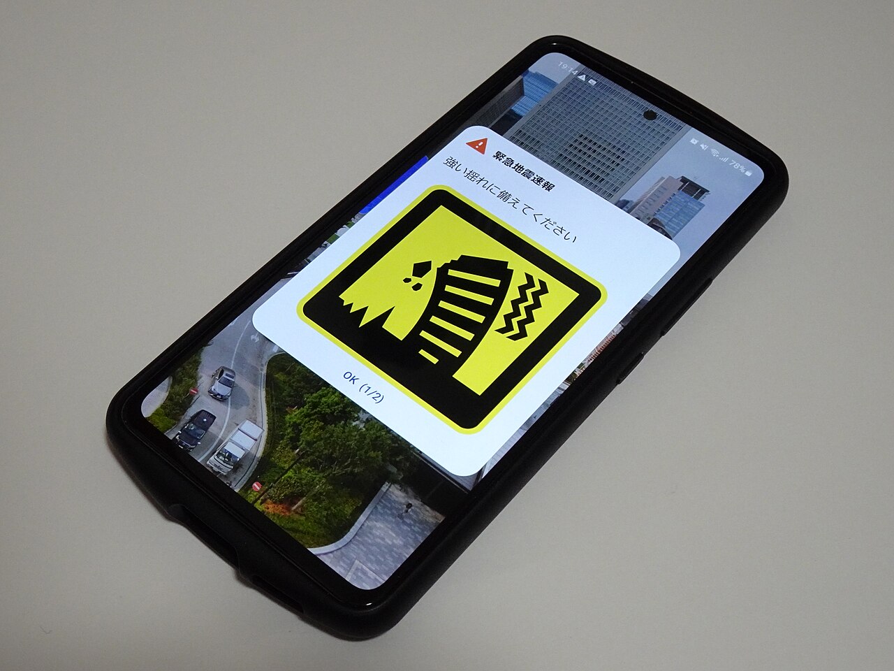 机の上に置かれたスマートフォンに緊急地震速報の通知画面が表示されている接写。