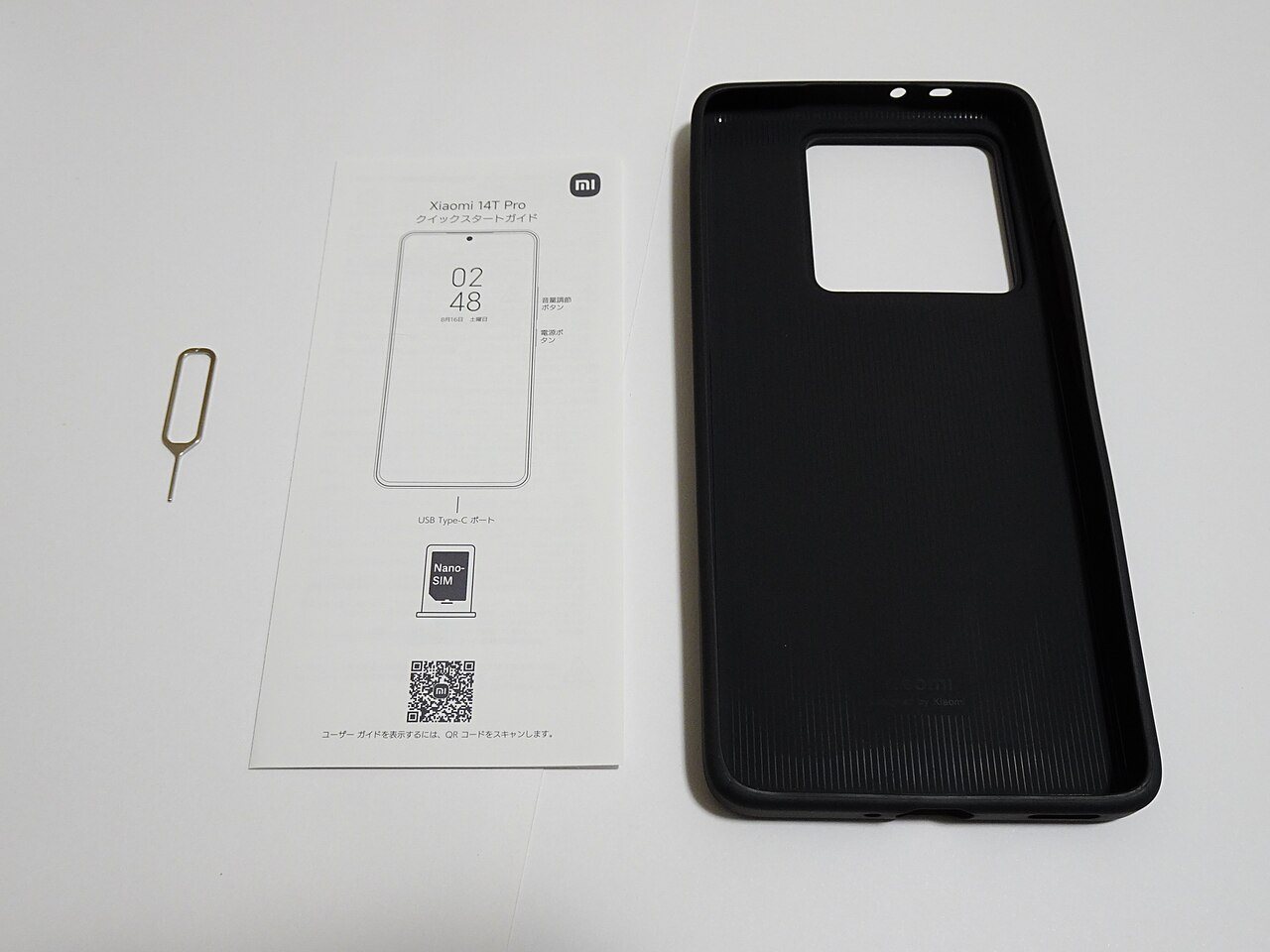スマートフォンの説明書とケース、SIMピンを机に並べた室内写真
